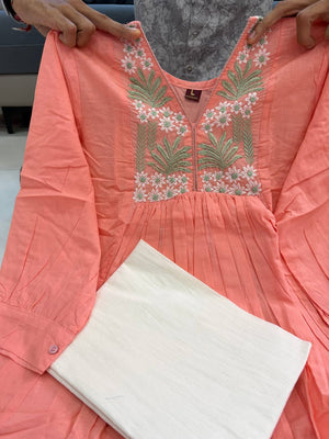 [actual-product] A coral pink cotton kurta with green and white floral embroidery on the chest, held up by a person's hands with a folded cream-colored fabric accessory.